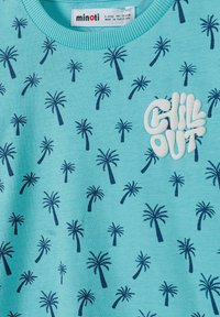 Sudadera de color azul claro con un patrón de palmeras en azul marino y un parche de texto blanco que dice "CHILL OUT". Hecha de algodón suave y texturizado.