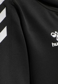Top sportivo nero con una texture liscia, caratterizzato da strisce diagonali bianche e un logo. Il tessuto sembra leggero e traspirante.