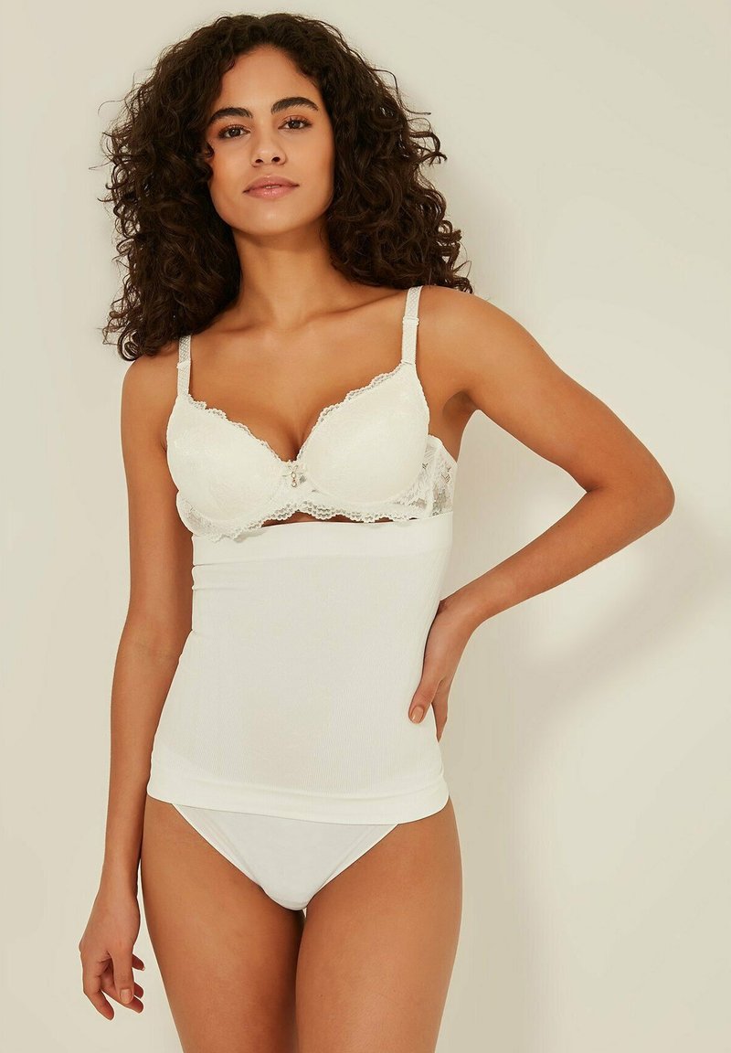 Weißer BH mit Spitzenbesatz und weißes, figurbetontes Shapewear-Top mit glatter Textur und nahtlosem Design. Schlichte, klare Linien.