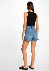 Shorts in denim, azzurri chiari, vestibilità rilassata con orlo sfilacciato, cinque tasche e cuciture a contrasto. Abbinati a un top senza maniche nero.