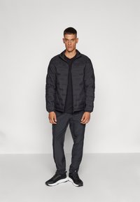 Black padded jacket with a textured design, paired with a black t-shirt and dark gray pants, worn with black sneakers.