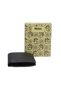 Billetera de cuero negro con costuras visibles, parcialmente abierta, colocada frente a una caja beige con un patrón que presenta diseños florales y una etiqueta de marca.