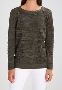 Kaki grön texturerad tröja med rundad halsringning, ribbade ärmslut och nederkant, med olika stickmönster och en avslappnad passform.