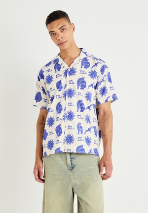 Short-sleeve button-up shirt in cream fabric featuring a repetitive blue pattern of stylized faces and sun motifs. Casual fit with collar.