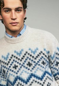 Pulover tricotat în crem, cu un model geometric în nuanțe de albastru și negru. Dispune de un guler ribotat și o textură moale.