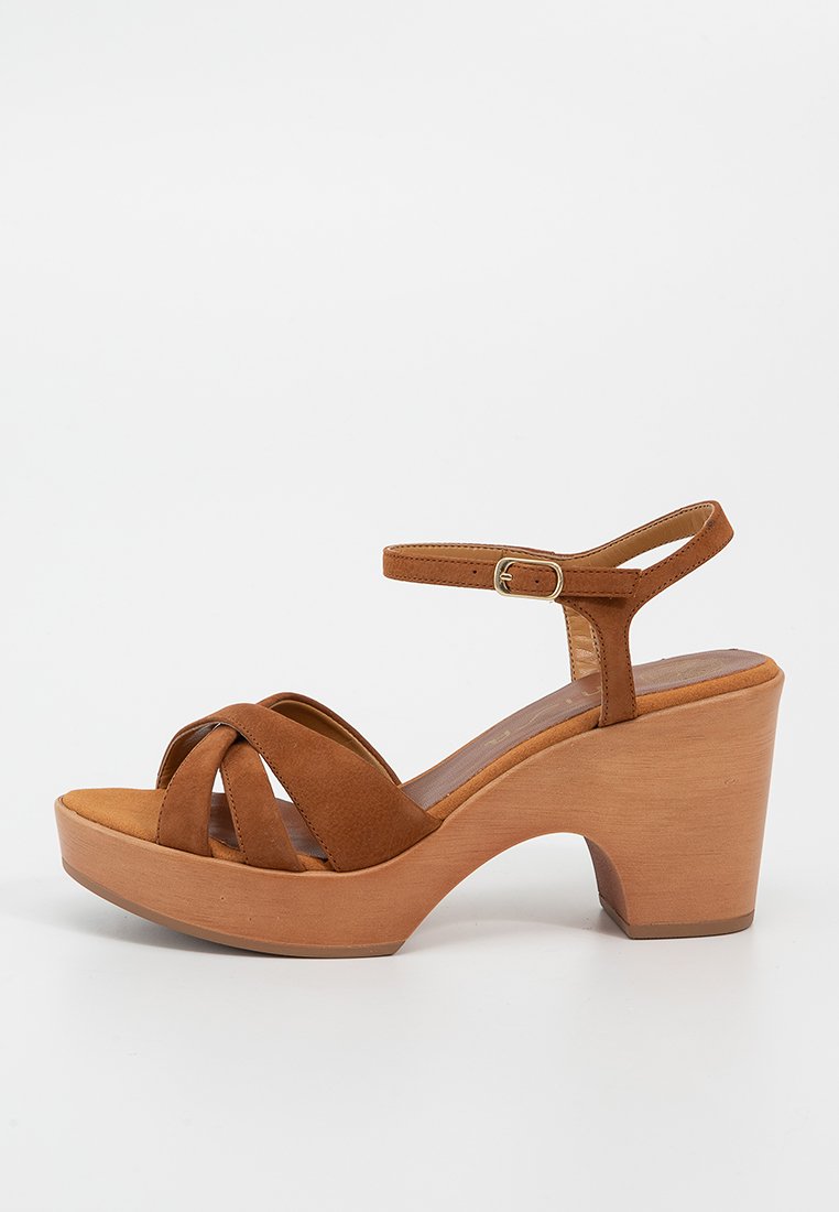 Sandale ouverte en suede marron avec un talon bloc en bois, une bride à la cheville et une fermeture à boucle sur fond blanc.