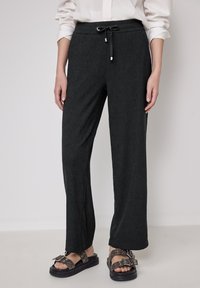 Zwarte joggers met een licht getextureerde stof, elastische tailleband en trekkoorddetail. Gecombineerd met chunky, gestudde sandalen.
