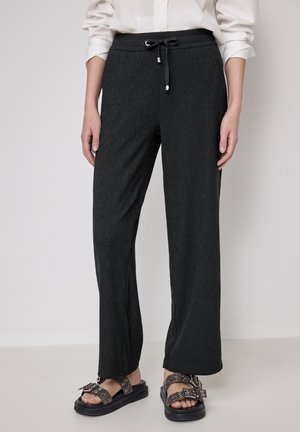 Pantaloni da jogging neri con un tessuto leggermente texturizzato, vita elastica e dettaglio con coulisse. Abbinati a sandali chunky con borchie.
