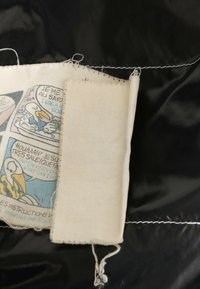 Étiquette en tissu usée avec des instructions de lavage en dessin animé décolorées cousues sur un tissu de vêtement noir brillant avec une couture blanche.