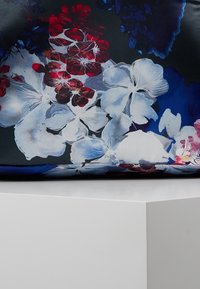 Kangas, jossa on tumma pohja ja suuret valkoiset, punaiset ja siniset kukkakuviot, lepää valkoisen pinnan kulmassa.