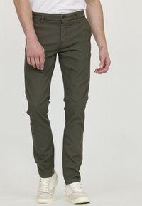 Chino ajusté vert avec une texture lisse, des poches avant et une fermeture à bouton. Associé à des baskets de couleur claire.