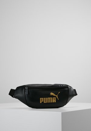 Schwarze Puma-Gürteltasche mit goldenem Logo und Reißverschluss, liegend auf einem weißen Podest vor einem schlichten grauen Hintergrund.