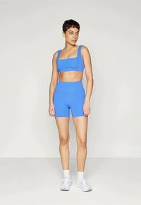 Μπλε αθλητικό σετ που περιλαμβάνει ένα τοπ κοντής γραμμής με πλατιές τιράντες και ψηλόμεσα σορτς, κατασκευασμένο από λείο ύφασμα με εφαρμοστή σχεδίαση.