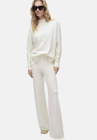 Crème lange mouwen top met een ronde hals, gecombineerd met wijde crème broek. Beide stukken hebben een zachte textuur en een relaxed fit.