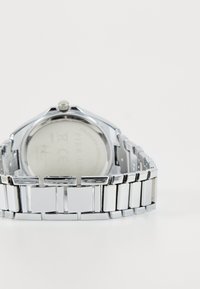 Montre en acier inoxydable argenté avec un bracelet en design rectangulaire, finition brillante et un fond de boîtier visible avec gravure.