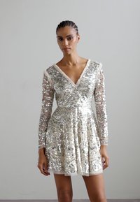 Paljetklänning med V-ringning och långa genomskinliga ärmar. Färg: silver. A-linjig silhuett med utsvängd nederdel. Texturerade dekorationer överallt.