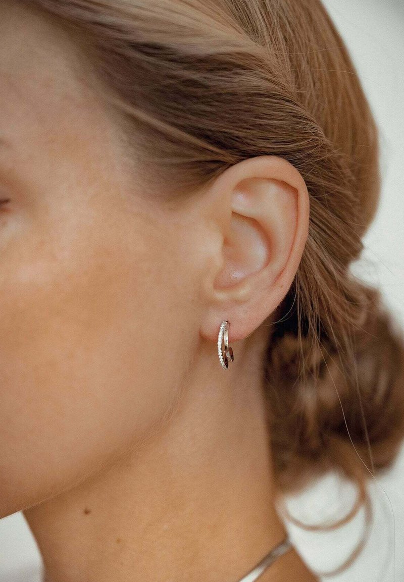 Boucles d'oreilles en argent avec un design torsadé et une surface texturée, ornées d'un petit accent en pierre précieuse claire. Vue en gros plan.