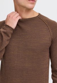 Brun ribbad stickad tröja med rund halsringning och raglanärmar. Materialet verkar mjukt med en subtil textur och en något dämpad nyans.