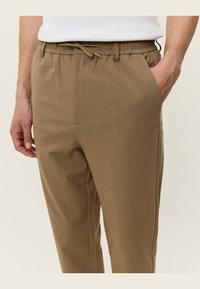 Pantalones marrones ligeros con cintura elástica y cordón, bolsillos laterales y una tela ligeramente texturizada. Corte ajustado con diseño de pierna recta.