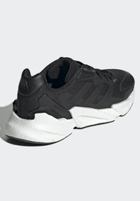 Zapatilla deportiva negra con un upper de malla texturizada, diseño de tres rayas y una suela acolchada blanca en contraste.