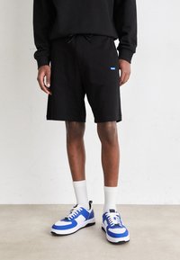 Shorts en coton noir avec une taille élastique, associés à des baskets bleu et blanc au design sportif et avec des accents à motifs.