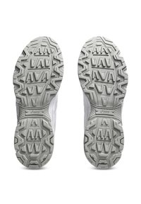 Zapatillas deportivas grises y blancas con suelas de goma texturizadas, que presentan un patrón de banda de rodadura geométrico para tracción y estabilidad.