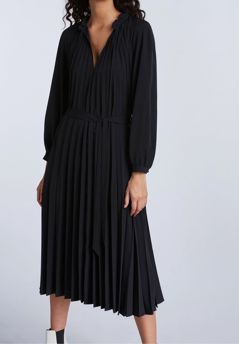 Robe noire plissée avec des manches longues, un décolleté en V profond et une taille cintrée. Composée d'un tissu léger avec une silhouette fluide.