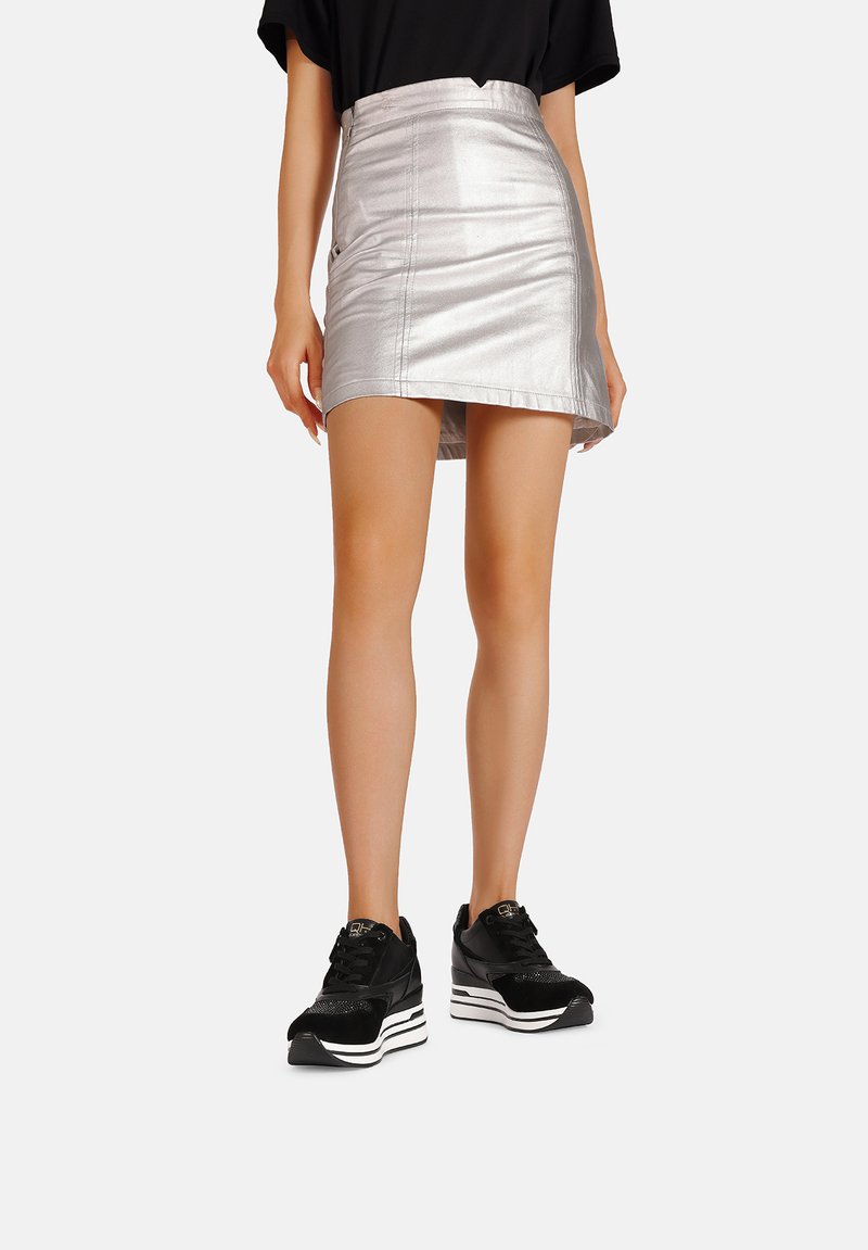 Gonna mini argentata metallizzata con un design aderente, caratterizzata da dettagli cuciti e un orlo dritto, abbinata a scarpe da ginnastica nere.