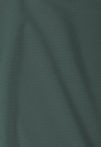 Tissu vert avec un motif texturé subtil et des plis doux créant des ombres et de la profondeur.