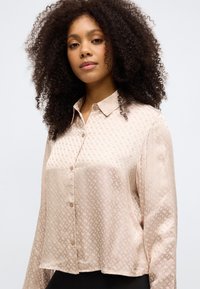 Ανοιχτό μπεζ πουκάμισο με κουμπιά, φτιαγμένο από απαλό ύφασμα με διακριτό γεωμετρικό μοτίβο. Διαθέτει γιακά και χαλαρή εφαρμογή.