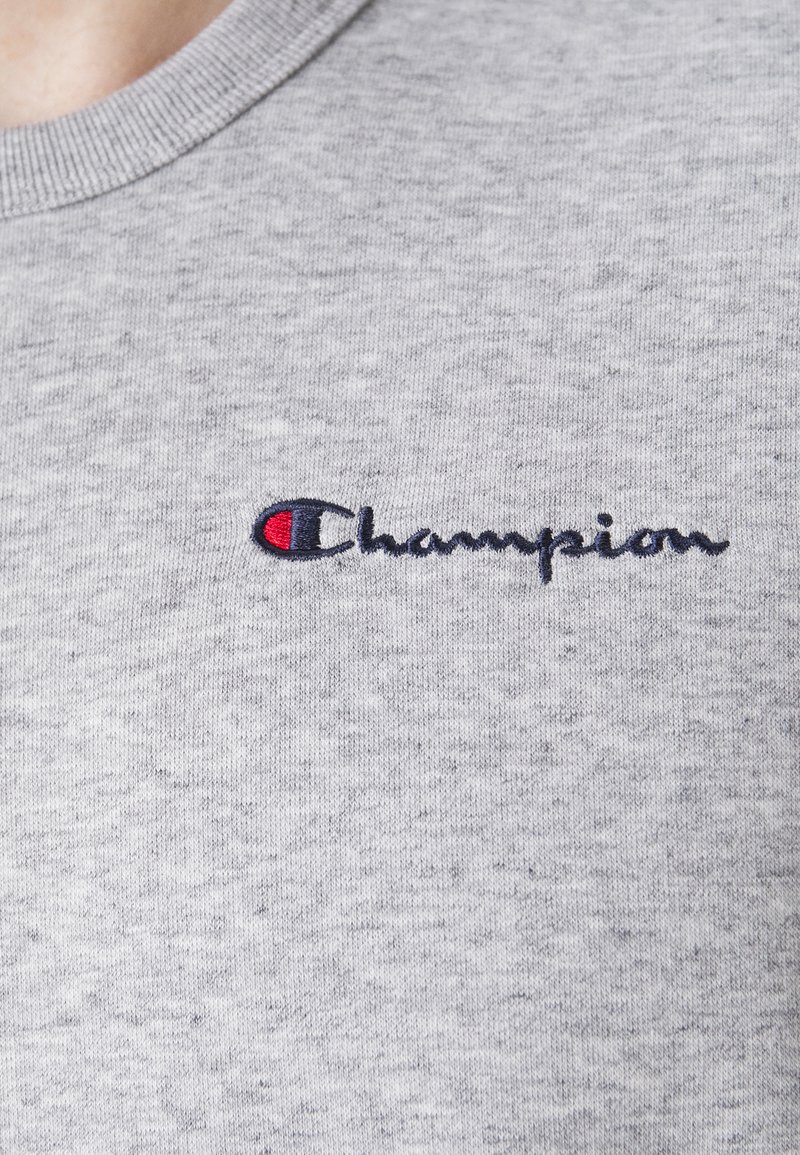 Sudadera gris con cuello redondo, hecha de tejido texturizado, que presenta un logotipo bordado de "Champion" en azul oscuro con un acento rojo.