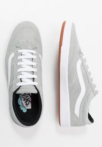 Baskets en daim gris avec des bandes latérales blanches, des lacets blancs et une semelle extérieure en caoutchouc naturel. Présentent une surface texturée et un intérieur rembourré.