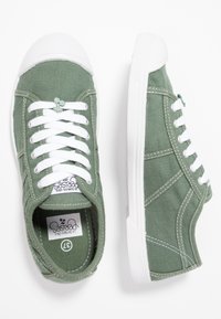 Sneakers di tela verde con punta e suola in gomma bianca, dotati di lacci bianchi e cuciture a contrasto. Include etichetta con logo all'interno.