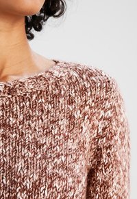 Gruby sweter dziergany na drutach w odcieniach brązu o fakturowanym, nierównym splocie. Szeroki dekolt, prążkowany dół oraz kremowe plamki w całej tkaninie.