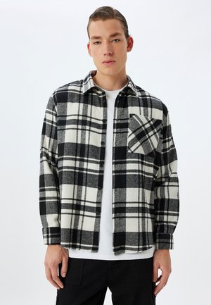 Zwart-wit geruite flanellen shirt met een knoopsluiting, lange mouwen en een borstzak met een visgraatpatroon.
