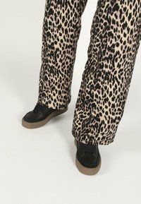 Pantaloni a gamba larga in stampa leopardata cream e nera, abbinati a sneakers nere con suola testurizzata e design con lacci.