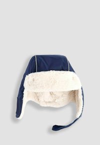 Námornícky modrá zimná čiapka s umelou kožušinou a ušnými chlopňami, jedna chlopňa voľne visiaca, na svetlo šedivom pozadí.