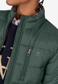 Chaqueta inflada verde con un cuello alto, con un interior burdeos, bolsillo con cremallera y un pequeño logo en el pecho.
