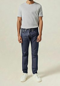 T-shirt gris à col rond, jean bleu foncé avec rivets en cuivre, et chaussures blanches à enfiler. Coupe ajustée, texture lisse, et design classique.