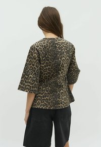 Leopardenmuster Peplum-Top mit 3/4-Ärmeln, aus einem strukturierten Stoff gefertigt, kombiniert mit schwarzen Denim-Shorts, von hinten betrachtet.