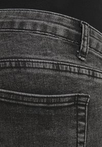 Jeans de denim preto com um acabamento desbotado, com um bolso traseiro e detalhes de costura visíveis. A cintura inclui passantes para cinto.