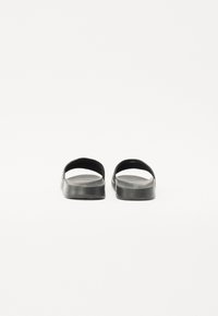 Sandale negre cu design deschis la spate, fabricate dintr-un material cauciucat neted. Talpă plată cu un model minim de profil și fără accesorii vizibile.