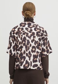Afskåret leopardmønstret skjorte i blød stof, med korte ærmer, krave og en løs pasform. Mønsteret inkluderer mørkebrune og beige pletter.