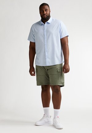 Cămașă bleu cu mâneci scurte și nasturi, asortată cu pantaloni scurți cargo verde măsliniu cu buzunare laterale, și adidași albi cu șosete albe.