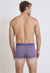 Jockey herrboxershorts i ett röd, blå och vit geometrisk mönster med en solid blå midja som har "JOCKEY"-logotypen.