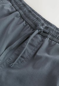 Pantalon gris foncé à taille élastique avec cordon de serrage noué et surpiqûres visibles sur les poches latérales sur un tissu lisse.