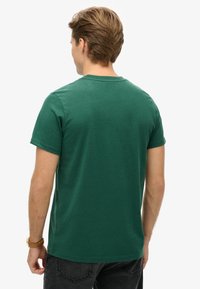 Grøn kortærmet t-shirt med rund hals, lavet af et blødt stof, der har en glat tekstur og en afslappet pasform. Vist fra bagsiden.