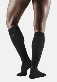 Calcetines de compresión negros, hasta la rodilla, fabricados con un material suave, con un puño acanalado y detalle del logo en el lateral.