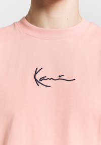 Růžové bavlněné tričko s kulatým výstřihem a krátkými rukávy. Na hrudi má vyšívaný námořnický modrý nápis "Kani". Měkká textura.