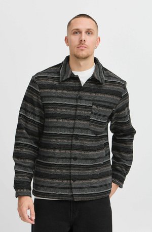 Black and gray patterned shirt jacket in woven fabric, featuring a collar, chest pocket, button closures, and long sleeves.